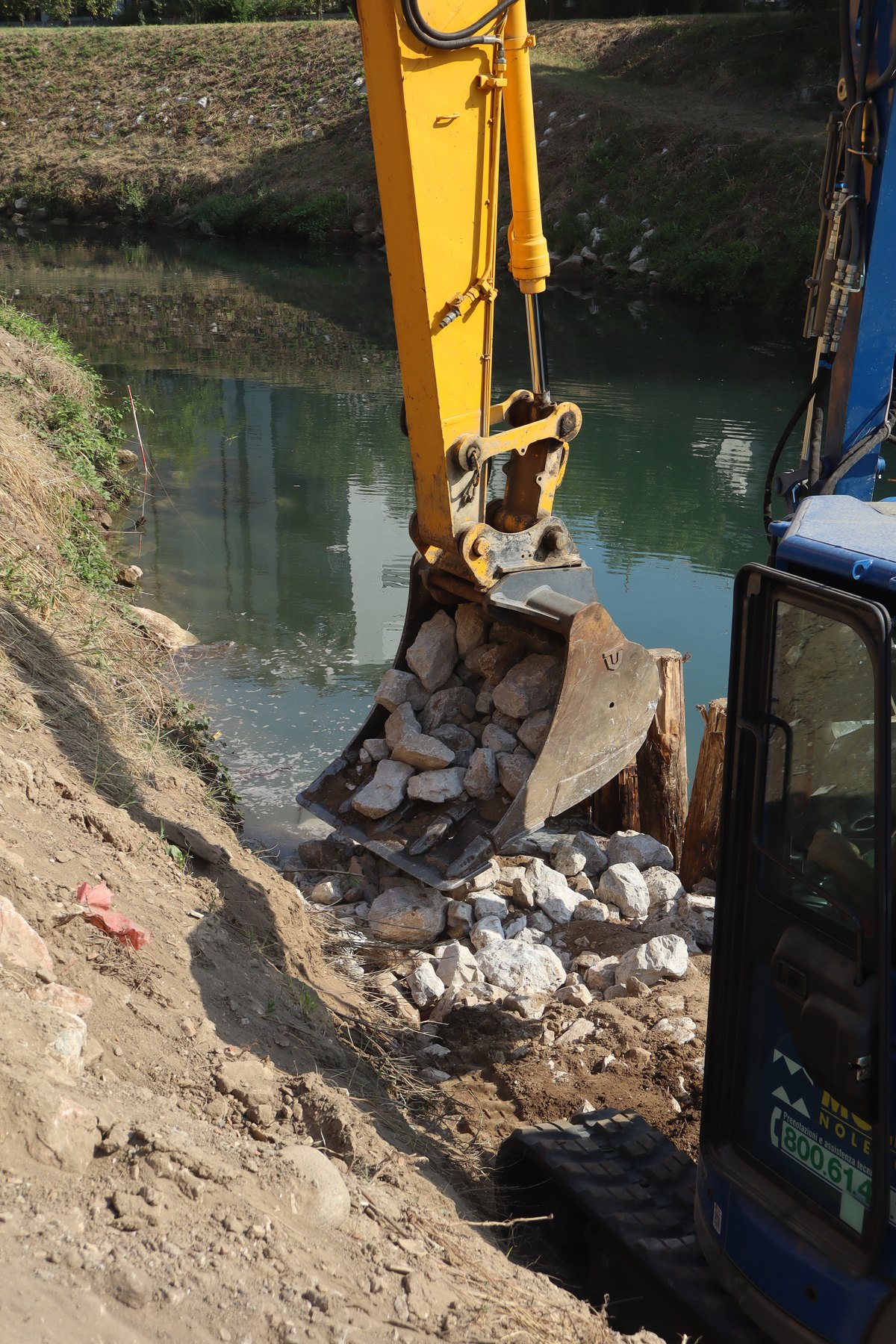 Escavatore che posa i massi di rinforzo sulla sponda del fiume